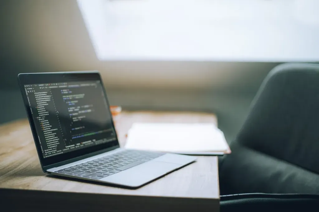 Laptop on a wooden desk showing lines of code in a dark editor