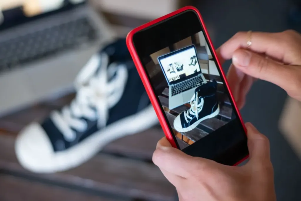 Person photographing a black canvas sneaker with a smartphone to create a listing