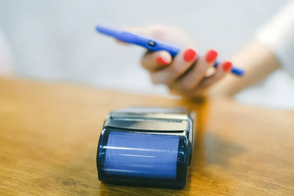 Hand holding a smartphone over a card payment terminal on a wooden counter