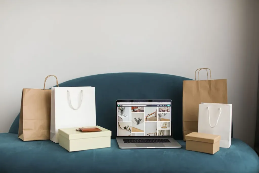 Laptop showing an online furniture shop on a blue sofa surrounded by shopping bags and boxes