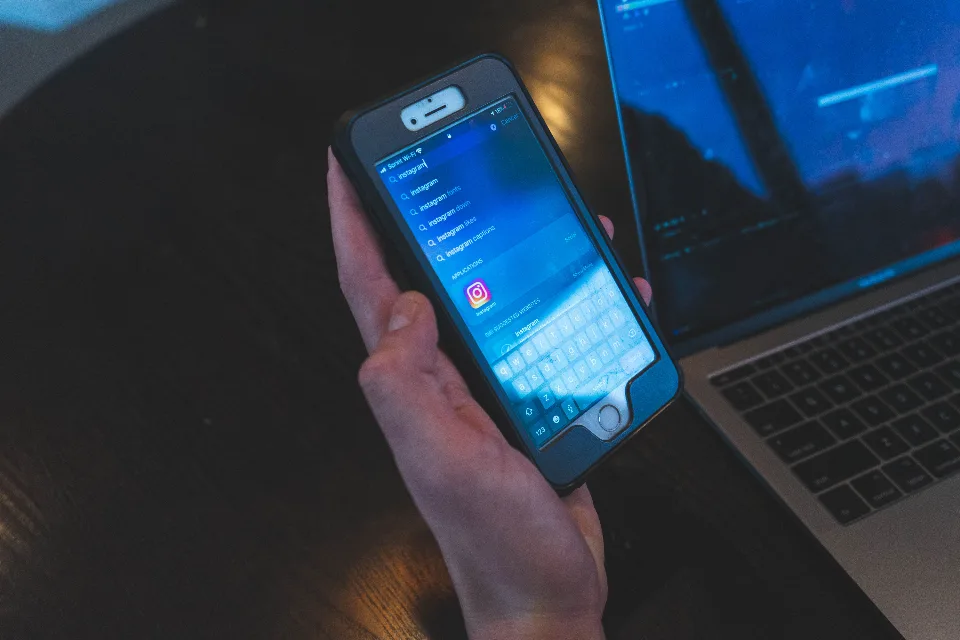 Person typing a prompt into an AI chat app on a smartphone next to a laptop
