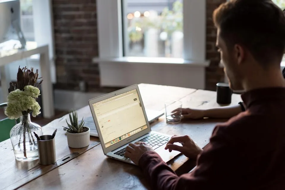 Man working on a laptop at a wooden desk deciding whether to upgrade his AI plan